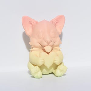 May include: A pastel pink, yellow, and green ceramic figurine of a dog holding a heart in its paws. The dog has a playful expression and its tongue is sticking out.