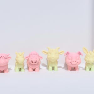 May include: A set of six small, pastel-coloured animal figurines. The figurines are made of a smooth, plastic-like material and are painted in shades of pink and yellow. The animals include a cow, a sheep, a goat, a pig, a horse, and a rabbit.