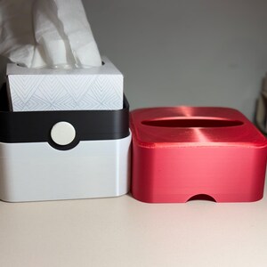 May include: Two tissue box holders. One is white with a black top and a white circular button. The other is a solid red box. The white box contains a tissue box with white tissues. The tissue box has a geometric pattern.