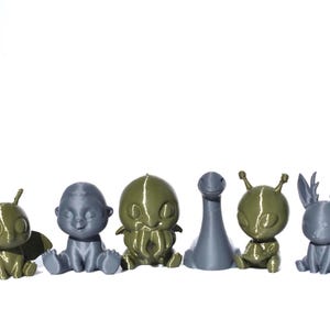Puede incluir: Una colección de seis figuras impresas en 3D en varios colores. Las figuras incluyen una polilla, un bebé, una criatura con tentáculos, un monstruo del lago Ness, un extraterrestre y una criatura parecida a un ciervo. Las figuras están dispuestas en fila.