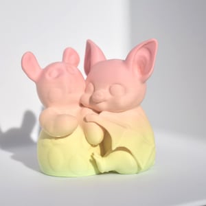 May include: A pair of pastel pink and yellow ceramic bat figurines. The bats are hugging each other.
