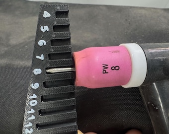 May include: A black ruler with white markings is used to measure the distance of a welding torch tip. The torch has a pink nozzle with the number 8 printed on it. The torch is black and has a white ring.