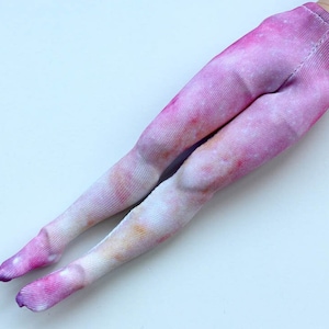 May include: Pink and white tie-dye leggings for a doll. The leggings have a galaxy print.