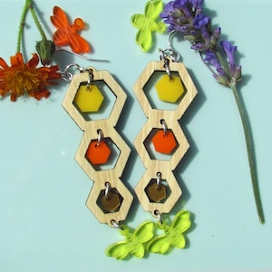 May include: A pair of wooden honeycomb earrings with dangling yellow, orange, and brown hexagonal charms. The earrings are accented with green butterfly charms.