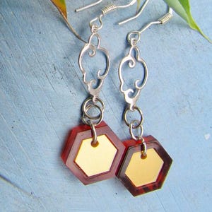 May include: A pair of dangle earrings with silver-toned filigree tops and red and gold hexagon-shaped pendants. The earrings have a geometric design and are suspended from silver-toned ear wires.