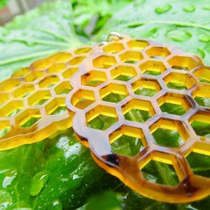 Puede incluir: Un par de pendientes de color ámbar con forma de panales de abeja. Los pendientes están hechos de un material translúcido y tienen un diseño delicado e intrincado.