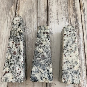 May include: Three triangular-shaped granite paperweights with a speckled pattern of black, white, and red.