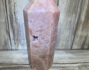 May include: A pink and white crystal point with a rough, natural texture. The point is a natural crystal formation and has a pointed tip.