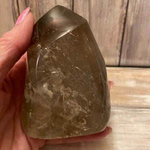 Könnte beinhalten: Eine klare, rauchige Quarzkristallspitze mit einer natürlichen, facettierten Form. Der Kristall ist durchscheinend und hat eine hellbraune Farbe.