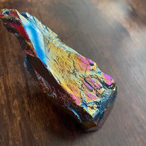 May include: A large, iridescent, dark grey crystal with a rough, textured surface. The crystal has a blue, purple, and gold sheen.