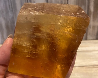 Può includere: Un grande cristallo di calcite chiaro e dorato di forma rettangolare. Il cristallo è traslucido e ha una leggera tonalità arancione.