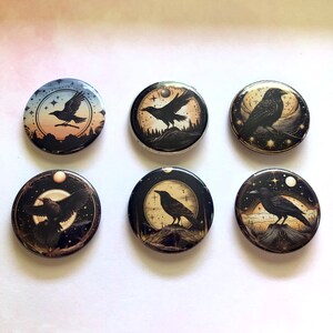 May include: Six round buttons featuring raven illustrations. Each button showcases a different design, including ravens in flight, perched on branches, or silhouetted against a night sky with stars and a full moon. The color palette includes black, white, and shades of brown.