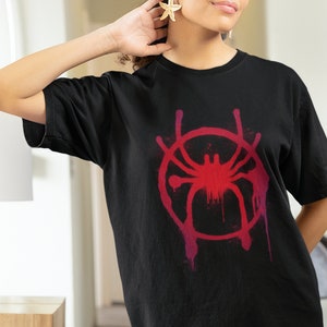 May include: Black t-shirt with a red and pink graphic of a spider in a circle. The graphic has a paint splatter effect.