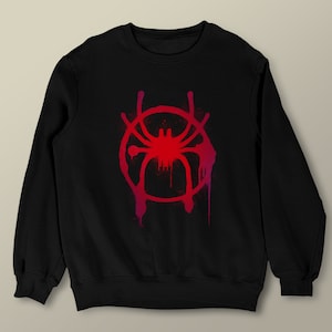 Puede incluir: Sudadera negra con un dise&ntilde;o de pintura en aerosol roja y rosa de una ara&ntilde;a en un c&iacute;rculo.