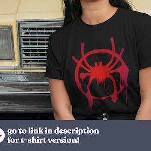 Puede incluir: Una camiseta negra con un gr&aacute;fico rojo y rosa del logotipo de Spider-Man: Into the Spider-Verse. El logotipo es una telara&ntilde;a estilizada con una ara&ntilde;a en el centro.