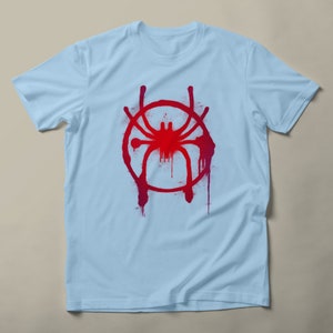 May include: Light blue t-shirt with a red and pink spray paint design of a spider in a circle.