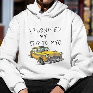 May include: White hoodie with a yellow taxi cab graphic and the text "I survived my trip to NYC".