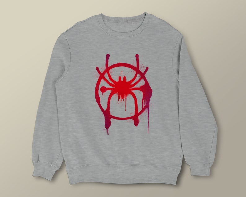 Puede incluir: Sudadera gris con un s&iacute;mbolo de Spider-Man rojo y rosa en la parte delantera. El s&iacute;mbolo es un c&iacute;rculo con una ara&ntilde;a dentro y tiene un efecto de pintura goteando.