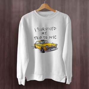 May include: White sweatshirt with the text "I survived my trip to NYC" and a cartoon yellow taxi cab.