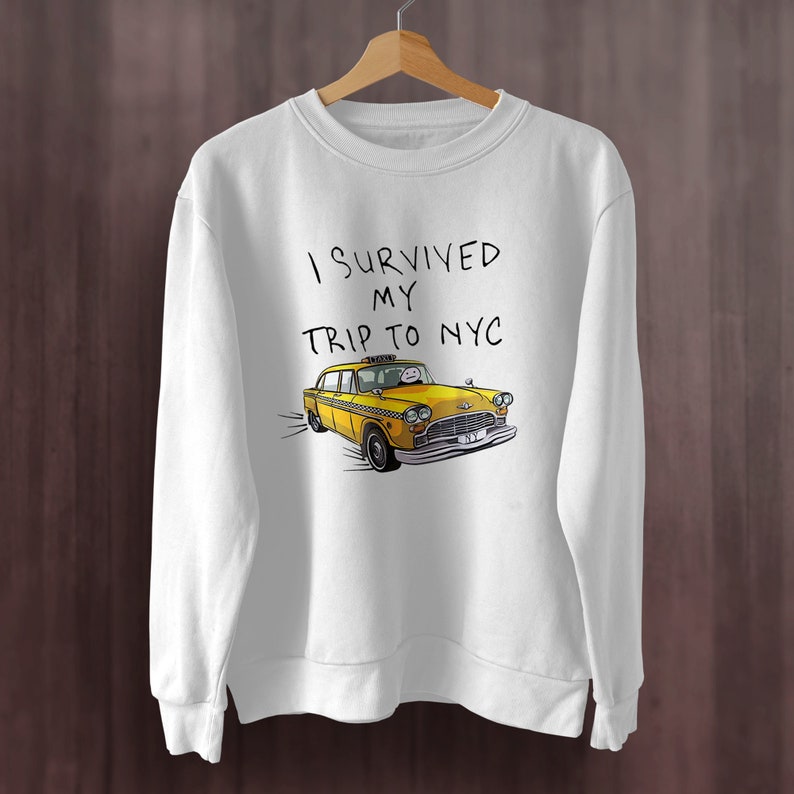 May include: White sweatshirt with the text "I survived my trip to NYC" and a cartoon yellow taxi cab.