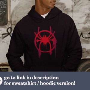 May include: A black hoodie with a red and pink stylized spider graphic. The graphic is in the shape of a circle with a spider in the center. The spider has eight legs and a red body. The hoodie has a drawstring hood and a kangaroo pocket.