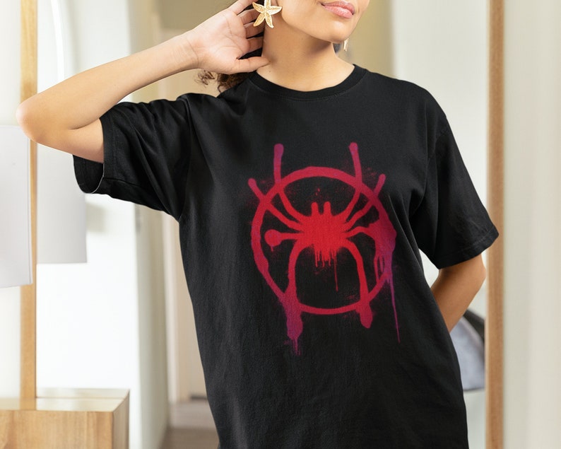 May include: Black t-shirt with a red and pink graphic of a spider in a circle. The graphic has a paint splatter effect.