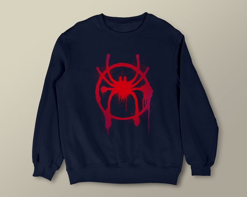 Puede incluir: Una sudadera azul marino con un gr&aacute;fico rojo y blanco de una ara&ntilde;a en un c&iacute;rculo. El gr&aacute;fico est&aacute; estilizado para parecer pintura en aerosol.