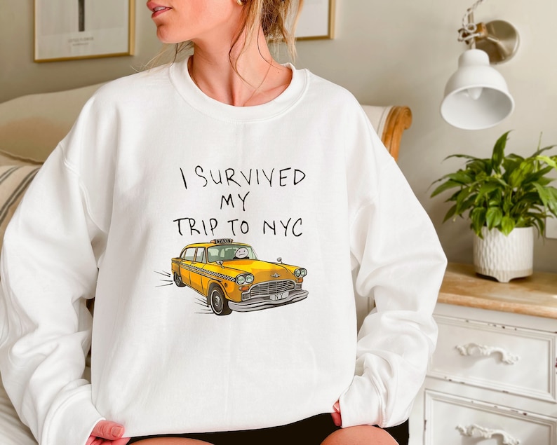 May include: White sweatshirt with the text "I survived my trip to NYC" and a yellow taxi cab illustration.