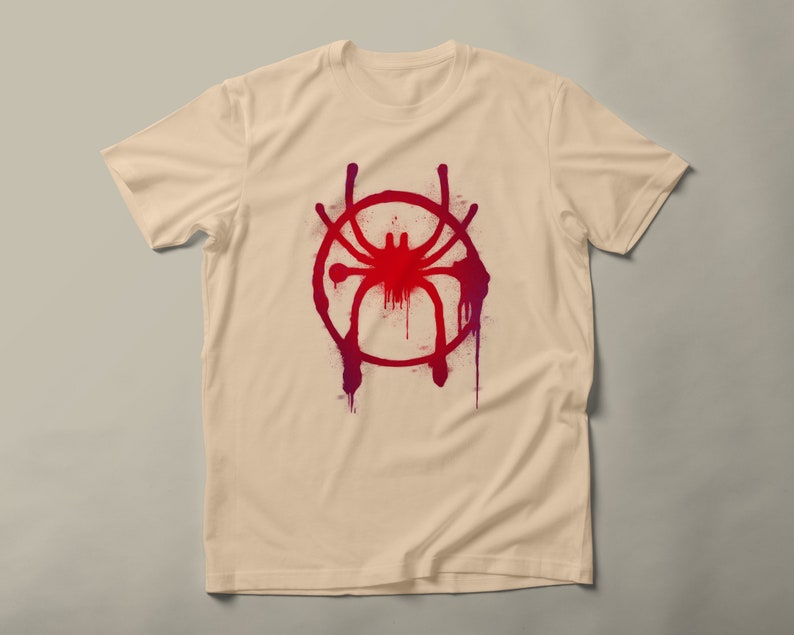May include: A beige t-shirt with a red and purple spray paint design of a spider in a circle.
