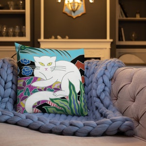 May include: A white cat with yellow eyes and a pink nose is depicted on a throw pillow. The cat is surrounded by colorful flowers and leaves on a blue background.
