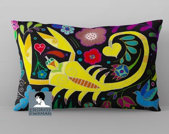 May include: A black pillow with a yellow scorpion design and colorful floral accents. The scorpion is surrounded by flowers, leaves, and a blue bird. The pillow has the text "THE DECORATED WOMAN" in the bottom left corner.