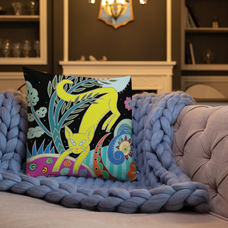 Peut inclure: Un chat jaune aux yeux noirs et au nez rose saute &agrave; travers un motif abstrait color&eacute; sur fond noir. Le motif comprend des feuilles vertes, des tourbillons bleus et des cercles roses et violets. L'oreiller est fait d'un tissu doux et est parfait pour ajouter une touche de fantaisie &agrave; n'importe quelle pi&egrave;ce.