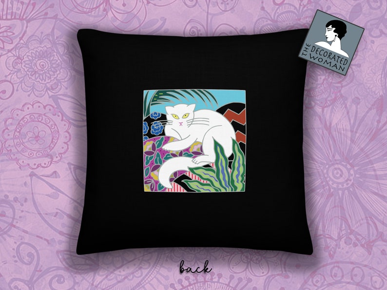 May include: Black throw pillow with a white cat illustration in a colorful, geometric design. The cat is lying down with its tail curled around its body. The design includes green, blue, pink, and yellow colors. The pillow has the text "The Decorated Woman" on the back.