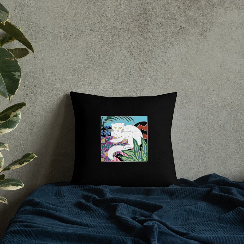 May include: A black throw pillow with a white cat illustration. The cat is lying down in a colorful, abstract floral pattern. The pillow is a great addition to any home decor.