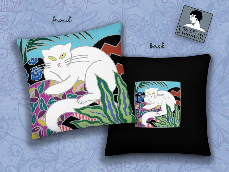 May include: A white cat with yellow eyes is lying on a colorful floral pattern. The cat is surrounded by green leaves and a blue sky. The pillow is black with a white cat on a colorful floral pattern. The pillow has the text "The Decorated Woman" on it.