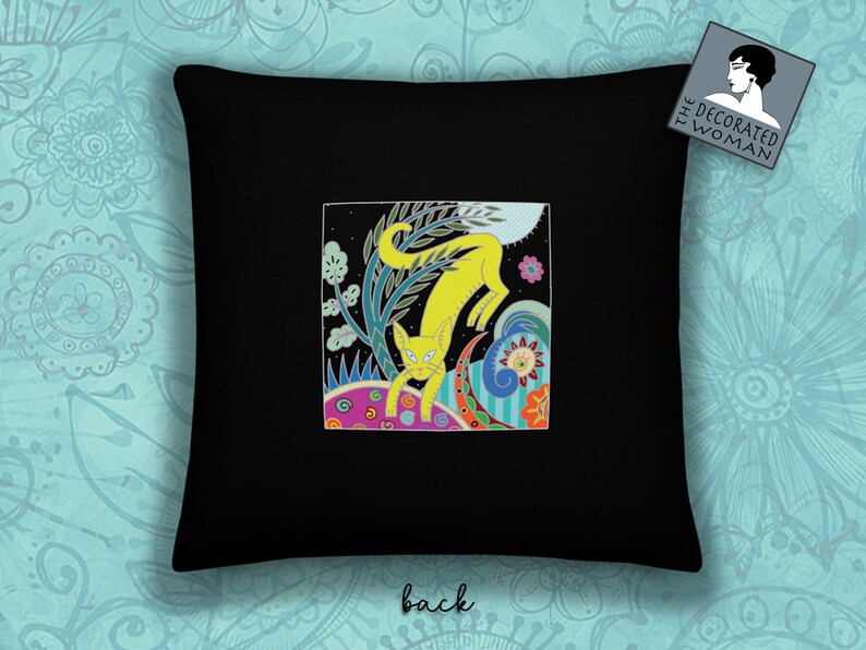 Peut inclure: Un oreiller noir avec une illustration color&eacute;e d'un chat jaune dans un jardin fantaisiste. Le texte "The Decorated Woman" est sur une &eacute;tiquette blanche dans le coin sup&eacute;rieur droit.