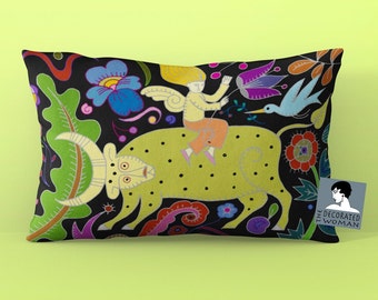 May include: A colorful pillow with a black background featuring a green bull with yellow spots, a person riding the bull, and a variety of flowers and leaves. The text "THE DECORATED WOMAN" is in the lower right corner of the pillow.