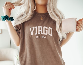 Może przedstawiać: Duża brązowa koszulka z białym napisem "VIRGO EST. 1994".