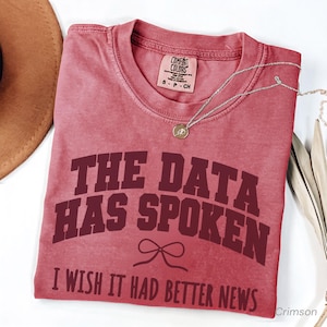 Op de afbeelding: Een vervaagd rood t-shirt met korte mouwen en een ronde hals. Het shirt heeft donkerrode tekst met de tekst THE DATA HAS SPOKEN, een kleine strik-afbeelding en de tekst I WISH IT HAD BETTER NEWS. Een Comfort Colors merklabel is zichtbaar.