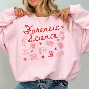Könnte beinhalten: Hellrosa Sweatshirt mit dem Schriftzug "Forensic Science" in roter Schrift, ergänzt durch rote Illustrationen von Gegenständen aus der Forensik, wie Handschellen und einer Lupe.
