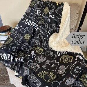 May include: A black and white fleece blanket with a crime scene theme. The blanket features a repeating pattern of crime scene tape, fingerprints, magnifying glasses, handcuffs, and a briefcase. The text "COZY VIB" and "CRIME SCENE DO NOT CROSS" are printed on the blanket. The blanket has a beige sherpa lining.