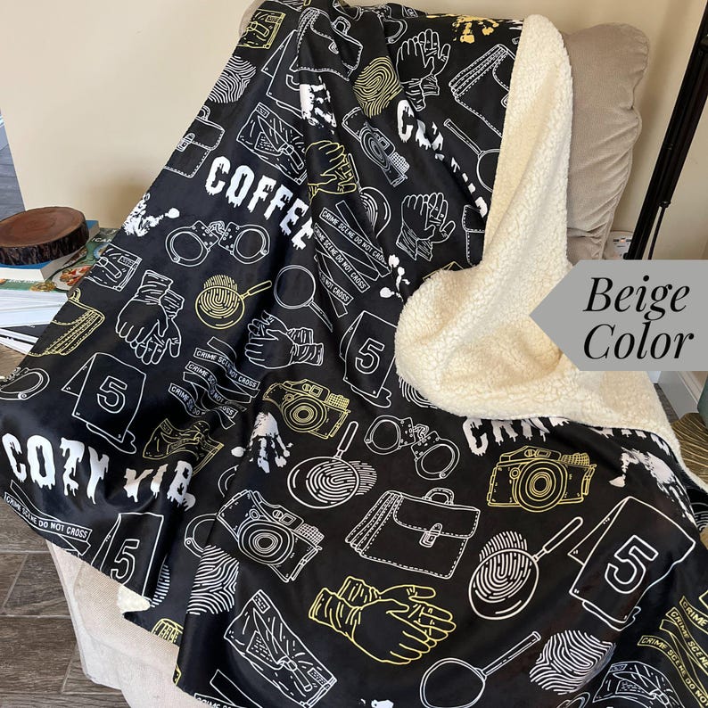 May include: A black and white fleece blanket with a crime scene theme. The blanket features a repeating pattern of crime scene tape, fingerprints, magnifying glasses, handcuffs, and a briefcase. The text "COZY VIB" and "CRIME SCENE DO NOT CROSS" are printed on the blanket. The blanket has a beige sherpa lining.
