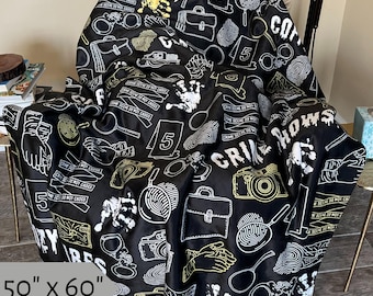 May include: Black and white throw blanket with a crime scene theme. The blanket features a repeating pattern of fingerprints, crime scene tape, handcuffs, cameras, and the words "Crime Scene Do Not Cross" and "Crime Shows". The blanket is 127 cm by 152 cm.
