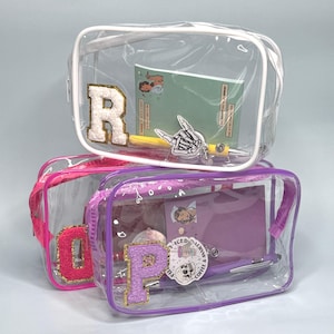 May include: Three clear, rectangular cosmetic bags with colored trim and zippers. Each bag contains stationery items. The bags have the letters "R", "O", and "P" on them. The bags are filled with pens, notebooks, and stickers.
