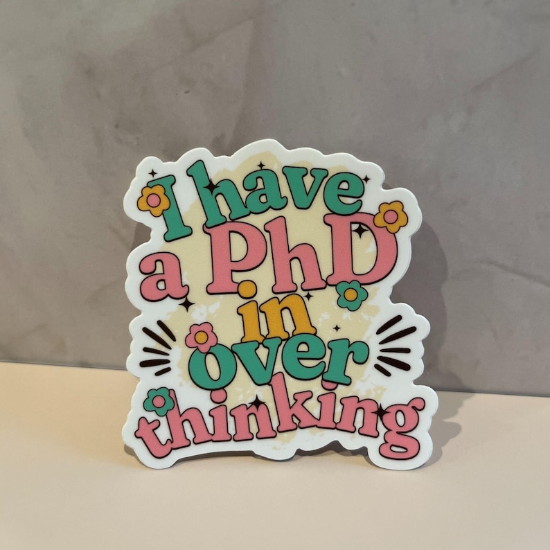 May include: A white sticker with the text "I have a PhD in over thinking" in pink, green, and yellow lettering with a flower design.