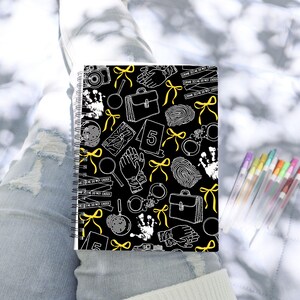 May include: A black spiral notebook with a white and yellow crime scene pattern. The pattern includes fingerprints, magnifying glasses, handcuffs, a briefcase, and crime scene tape. The text "CRIME SCENE DO NOT CROSS" is repeated on the tape.