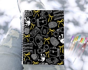 May include: A black spiral notebook with a white and yellow crime scene pattern. The pattern includes fingerprints, magnifying glasses, handcuffs, a briefcase, and crime scene tape. The text "CRIME SCENE DO NOT CROSS" is repeated on the tape.