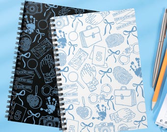 May include: Two spiral-bound notebooks with crime scene-themed patterns. One notebook has a black background with blue illustrations, while the other has a white background. The designs include magnifying glasses, fingerprints, and the text "DO NOT CROSS".