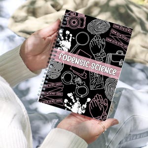 May include: A black spiral notebook with a white design featuring crime scene tape, fingerprints, handcuffs, a magnifying glass, and a camera. The text "FORENSIC SCIENCE" is written in pink on the front cover.