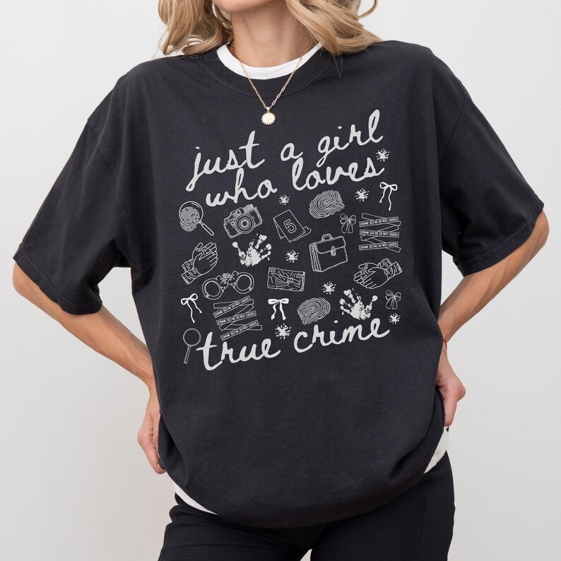 以下が含まれることがあります： 「just a girl who loves true crime」の白文字が入った黒いTシャツ。虫眼鏡、カメラ、手錠、指紋など、犯罪に関連するイラストが描かれています。